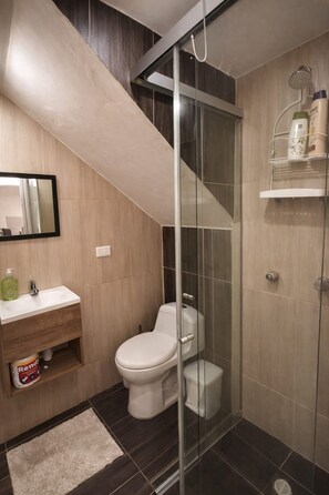 Un bagno moderno con box doccia in vetro, un water, un lavabo con specchio e uno scaffale con articoli da toilette.