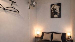 Ett sovrum med en säng, två sänglampor, en väggmonterad fläkt och en inramad tavla.