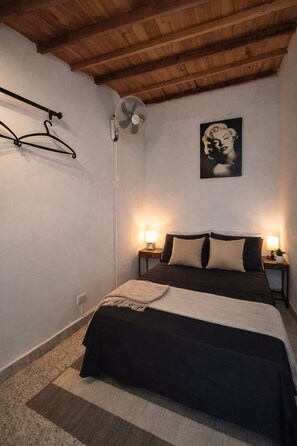 Una camera da letto con un letto, due lampade da comodino, una ventola a muro e un quadro incorniciato.