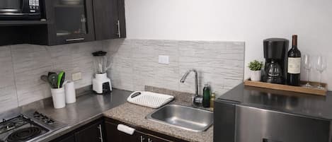Una cocina moderna con armarios oscuros, un refrigerador de acero inoxidable, un microondas, una cafetera y un lavabo.