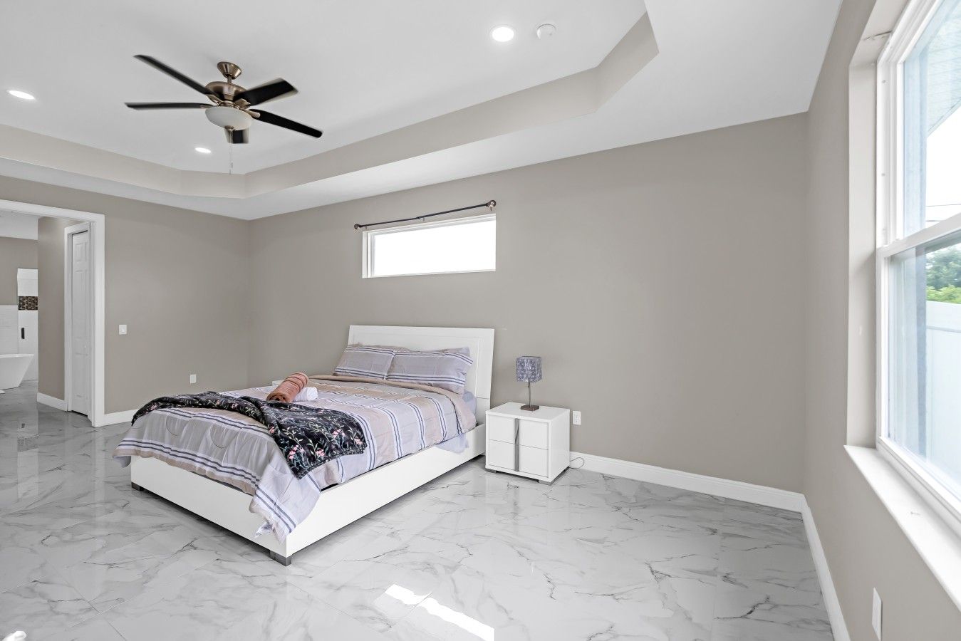A bedroom with a bed, a ceiling fan, a nightstand, and a window.