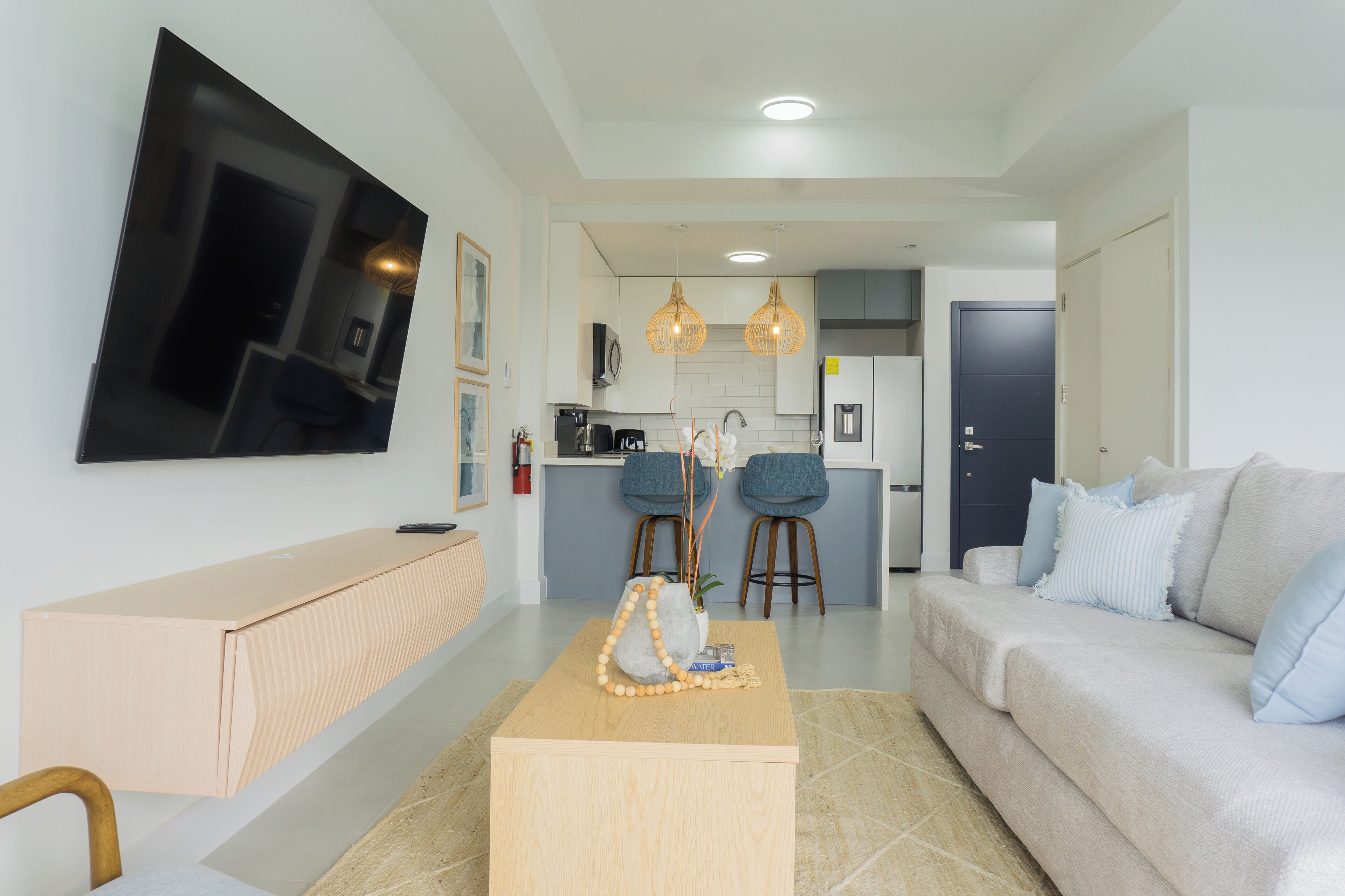 Een moderne woonkamer met een flatscreen televisie, een houten salontafel, een bank en een keuken op de achtergrond.