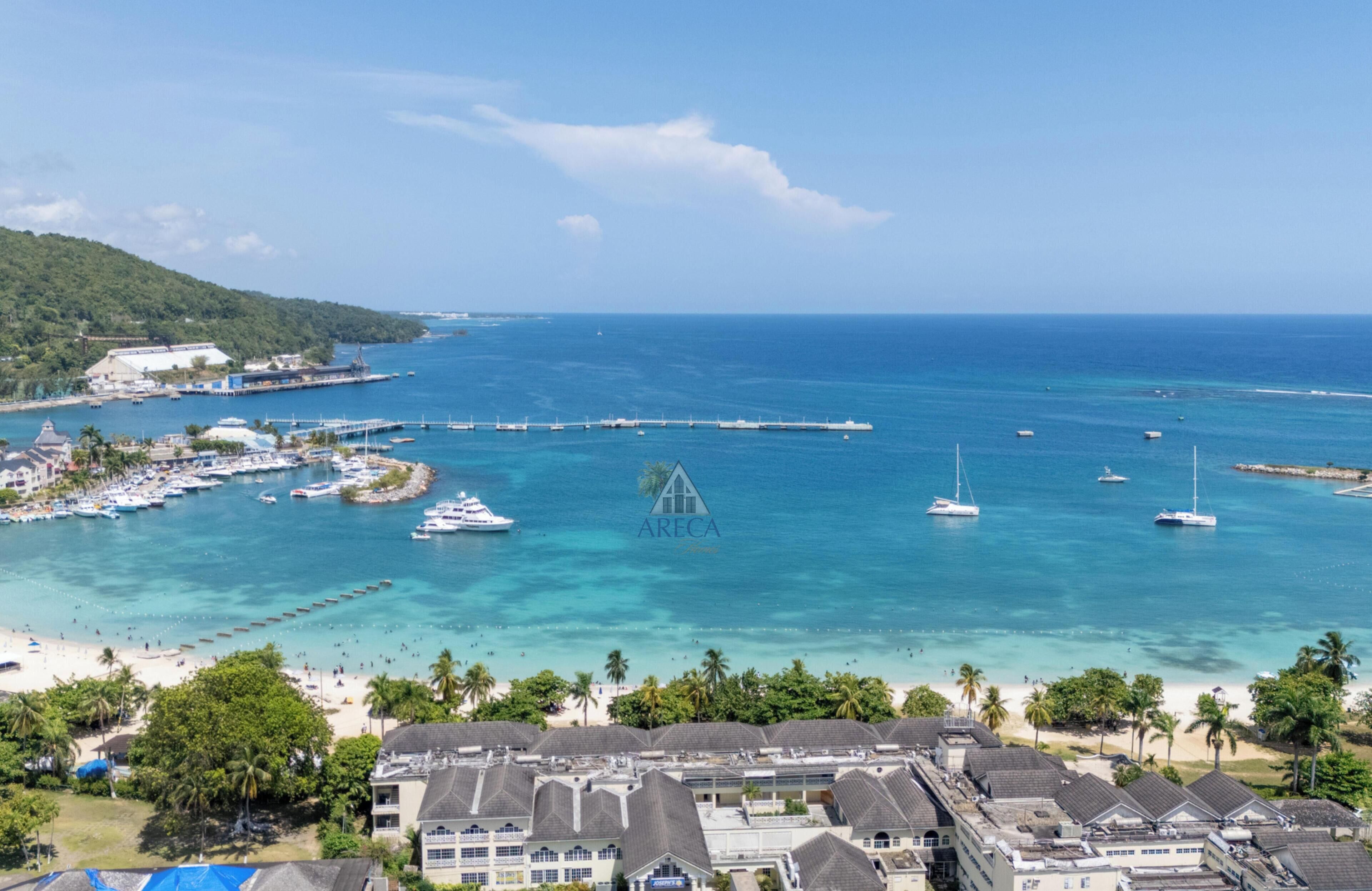 A coastal resort with multiple buildings, a marina with boats, and a beach.