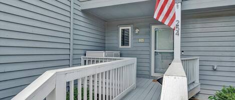 A residential building with a gray exterior, a white porch with a railing, and an American flag.
