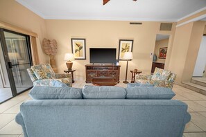 A living room with a grey sofa, two armchairs, a TV, and framed artwork on the wall. - Kapalua Golf Villa 25P7 Gold Ocean View 2BD/2BA (Lahaina)