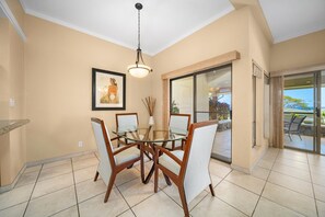 A dining area with a glass table and chairs, a ceiling light, a framed picture on the wall, and a sliding glass door leading to an outdoor space. - Kapalua Golf Villa 25P7 Gold Ocean View 2BD/2BA (Lahaina)