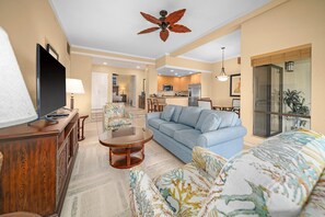 A living room with a sofa, armchair, coffee table, TV, and ceiling fan. - Kapalua Golf Villa 25P7 Gold Ocean View 2BD/2BA (Lahaina)