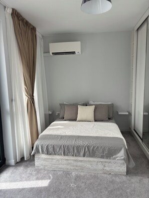 Une chambre moderne avec un grand lit, un ventilateur de plafond, un appareil de climatisation et une porte-fenêtre coulissante.