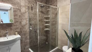 Une salle de bain moderne avec une douche en verre, un lavabo avec un miroir et une plante en pot.