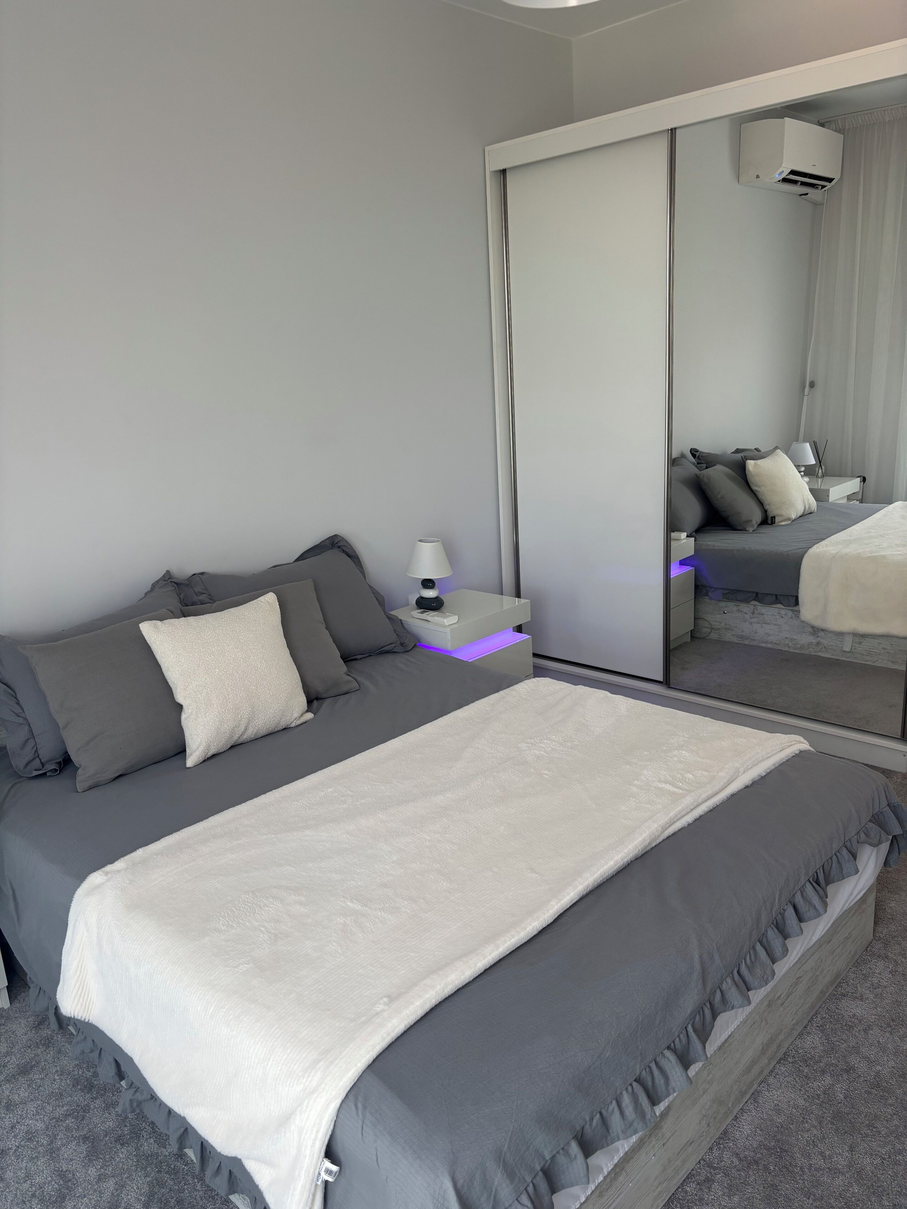 Une chambre à coucher moderne avec un grand lit, une table de chevet, une lampe et un miroir.