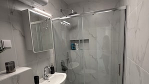 Moderni kylpyhuone, jossa on lasiseinällinen suihku, valkoinen pesuallas ja sen yläpuolella peili.
