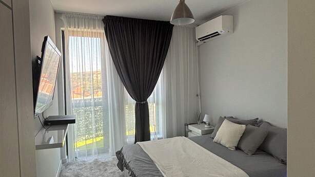 A modern hotel room with a bed, a desk, a television, and a window with curtains.