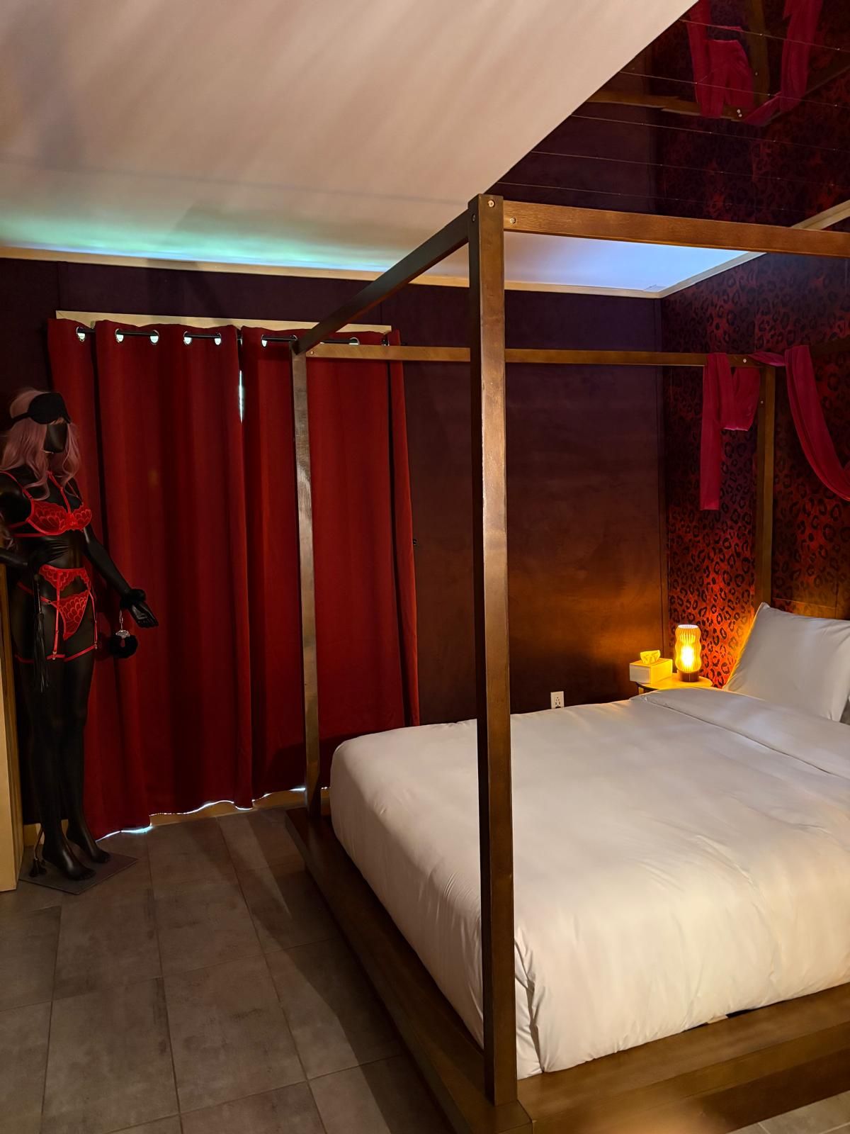 Ein Bett mit Baldachin, ausgestattet mit weißer Bettwäsche, ein Nachttisch mit Lampe und ein roter Vorhang.