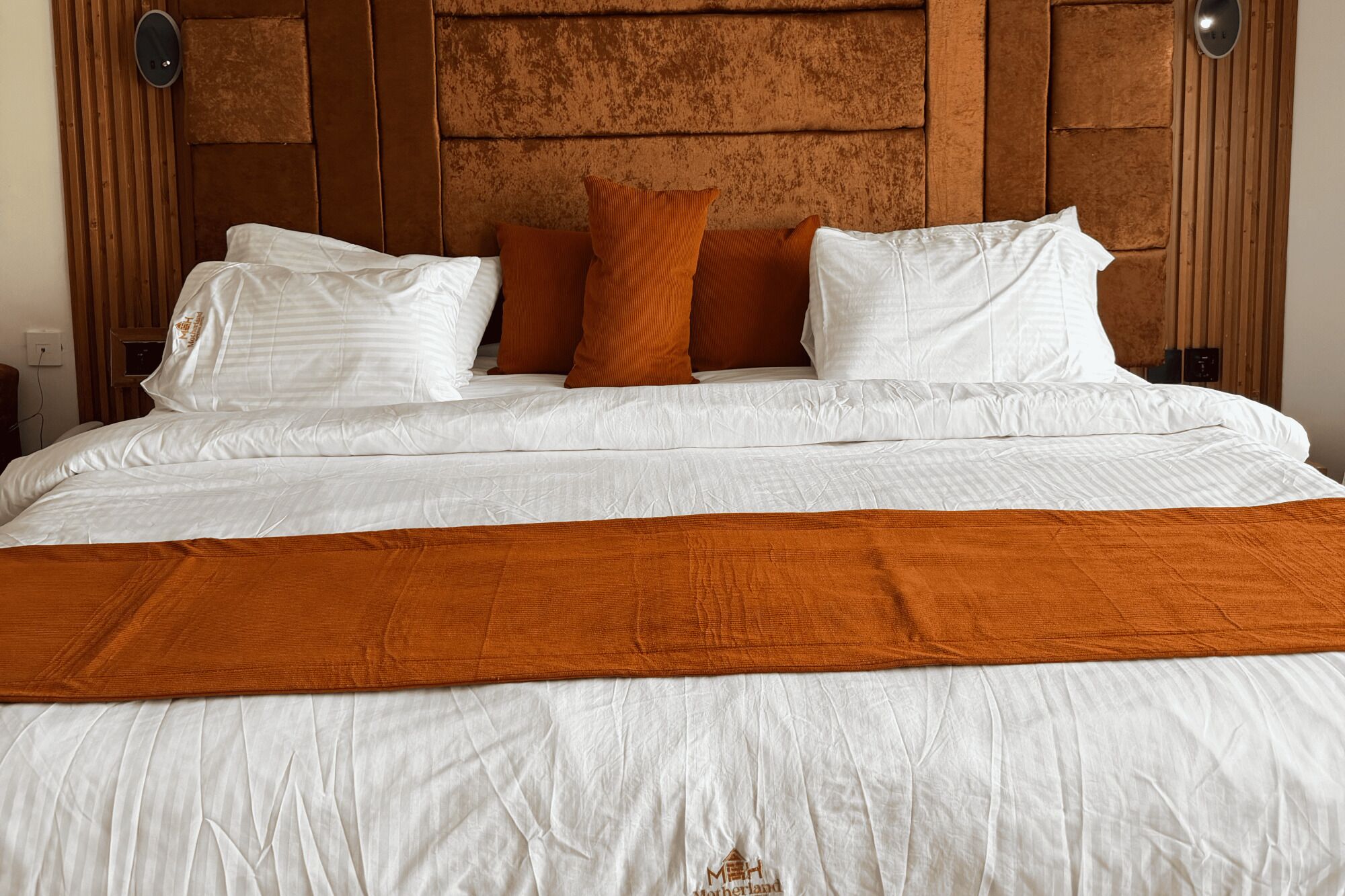 A neatly made bed with white bedding and a brown throw blanket.