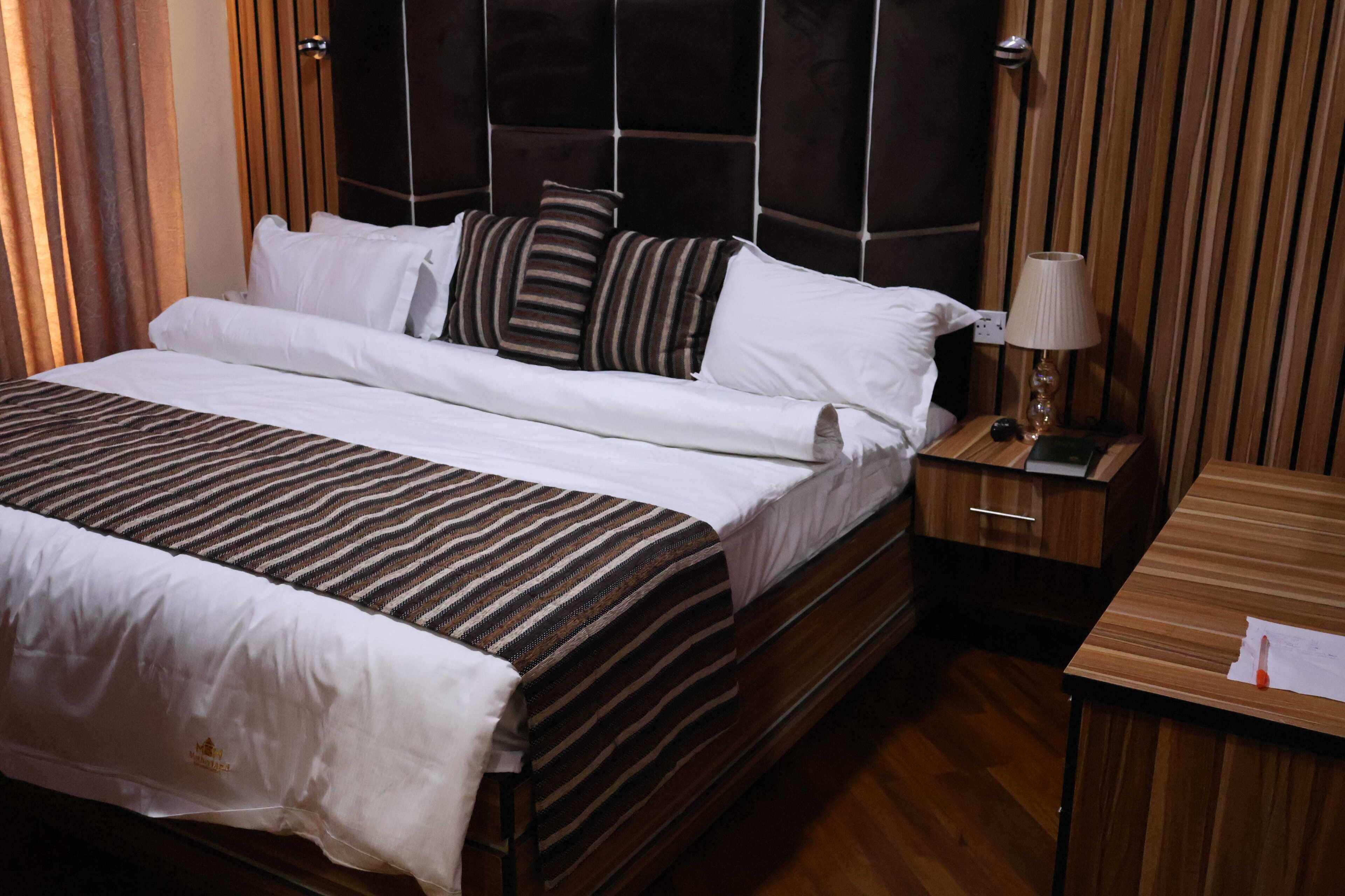 Une chambre d’hôtel avec un grand lit, une tête de lit en bois et une table de chevet avec une lampe.