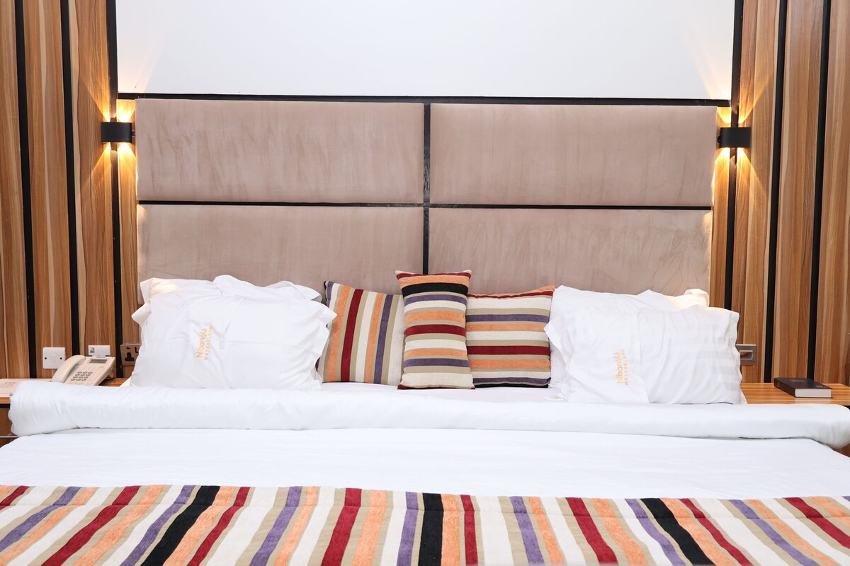 Una habitación de hotel con una cama grande, varias almohadas, una alfombra a rayas y paneles de madera en las paredes.