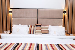 Una habitación de hotel con una cama grande, varias almohadas, una alfombra a rayas y paneles de madera en las paredes.