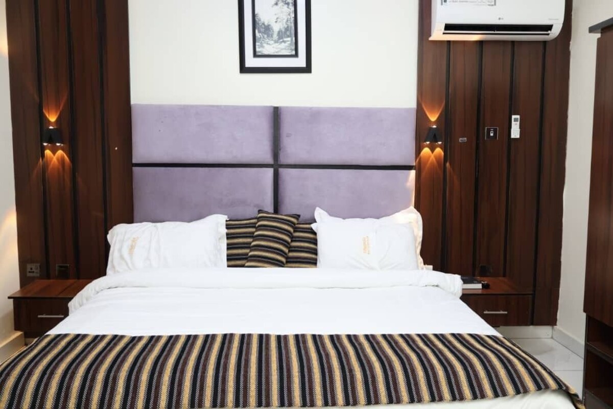 Habitación de hotel con cama, mesitas de noche, cabecero, luces empotradas en la pared y equipo de aire acondicionado.