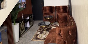 Una sala de estar con un sofá de terciopelo marrón, una mesa de centro negra y dorada, y una mesita redonda con base dorada.