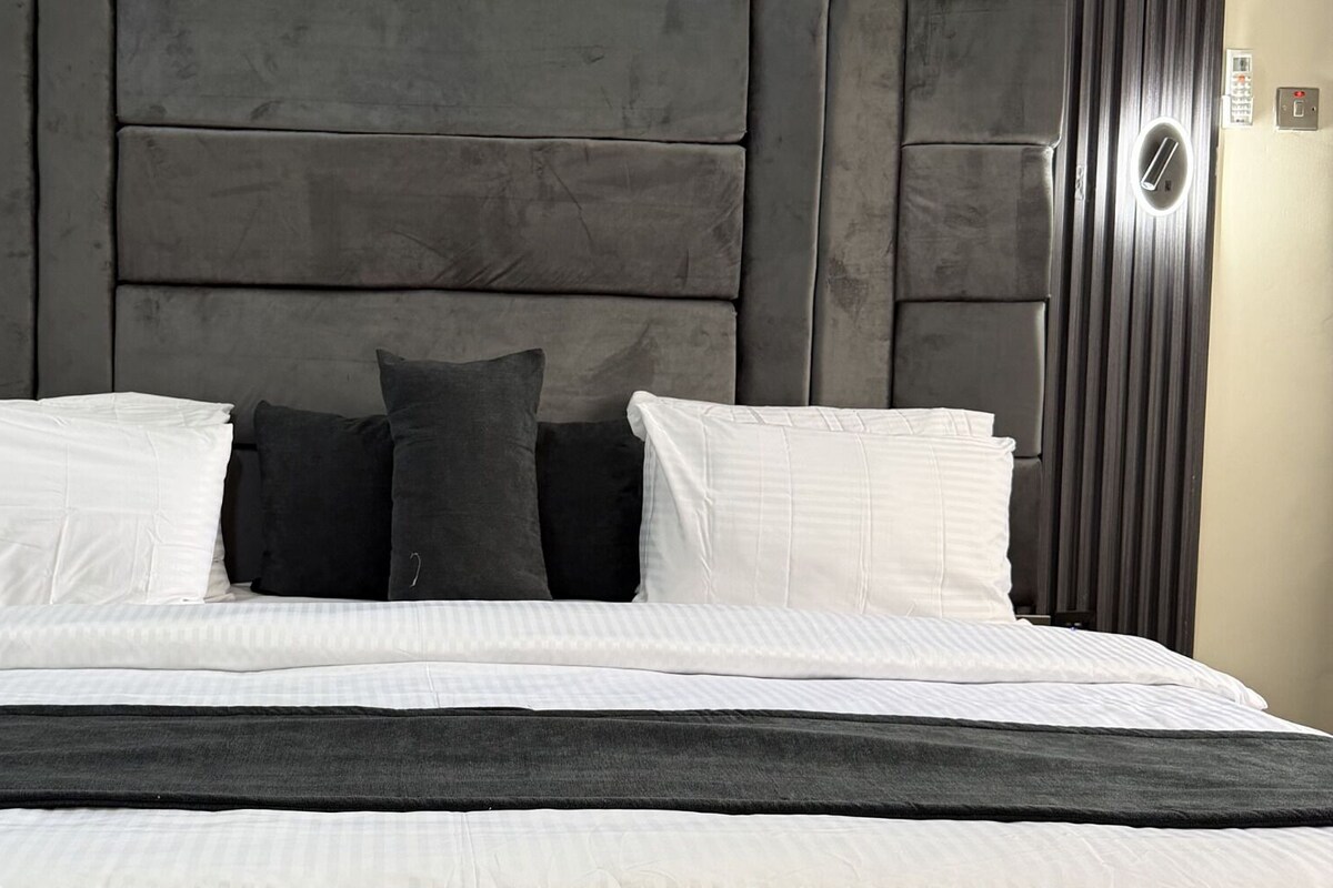Una cama con cabecera oscura, almohadas blancas y oscuras, y una manta negra.
