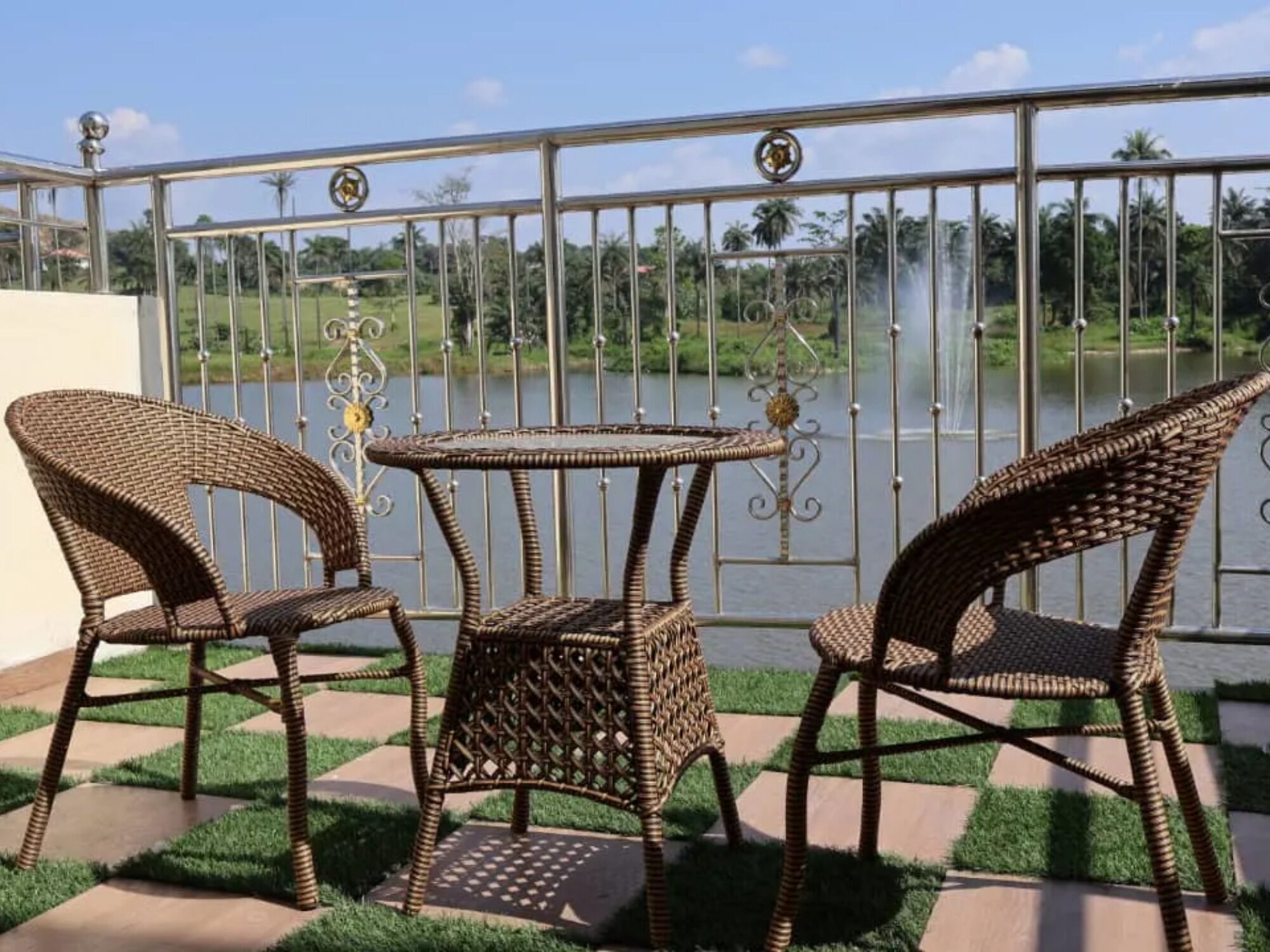 A balcony with wicker furniture, a small table, and a metal railing overlooking a body of water.