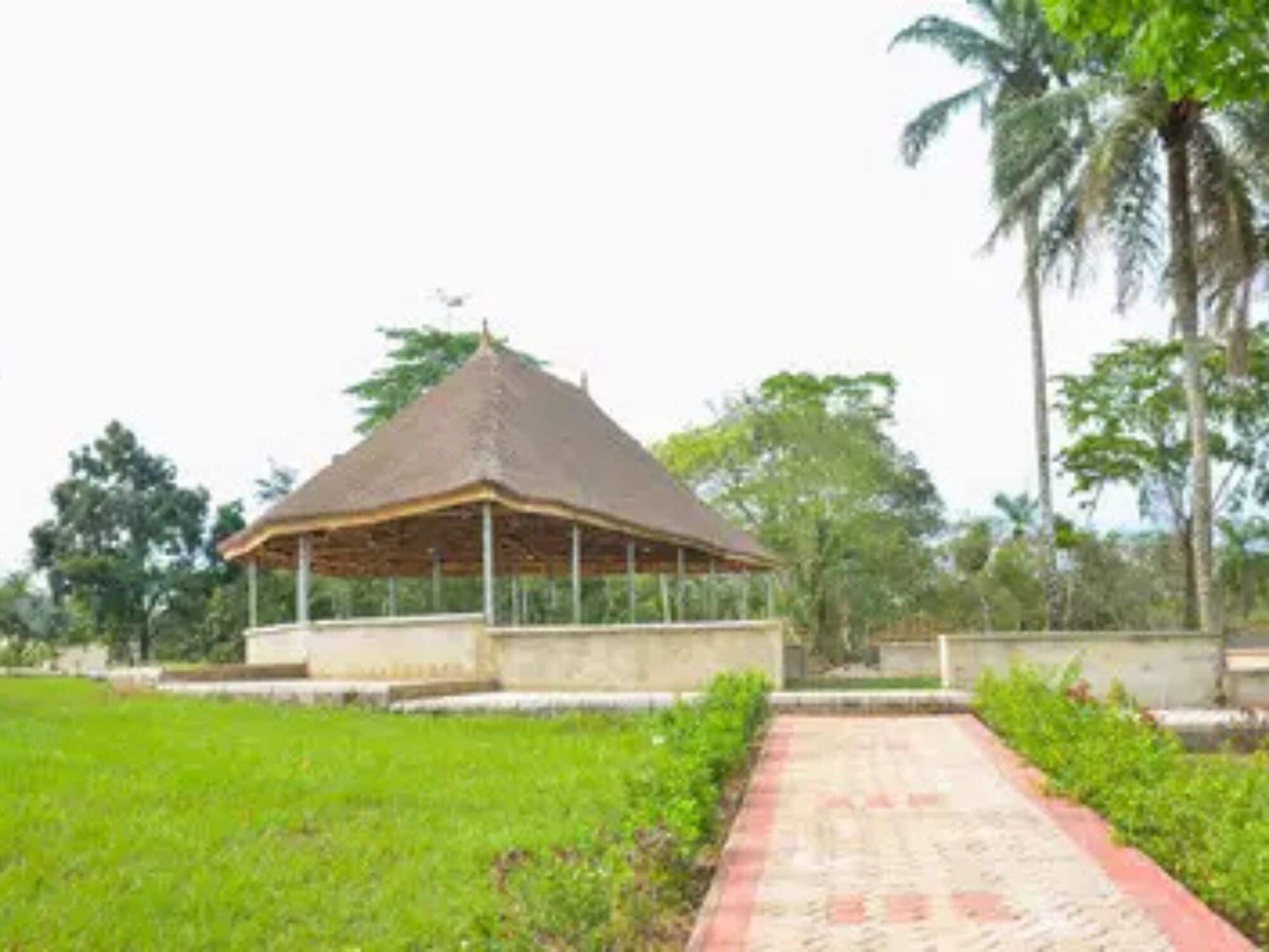 A pavilion with a thatched roof, surrounded by a well-maintained lawn and a paved pathway.