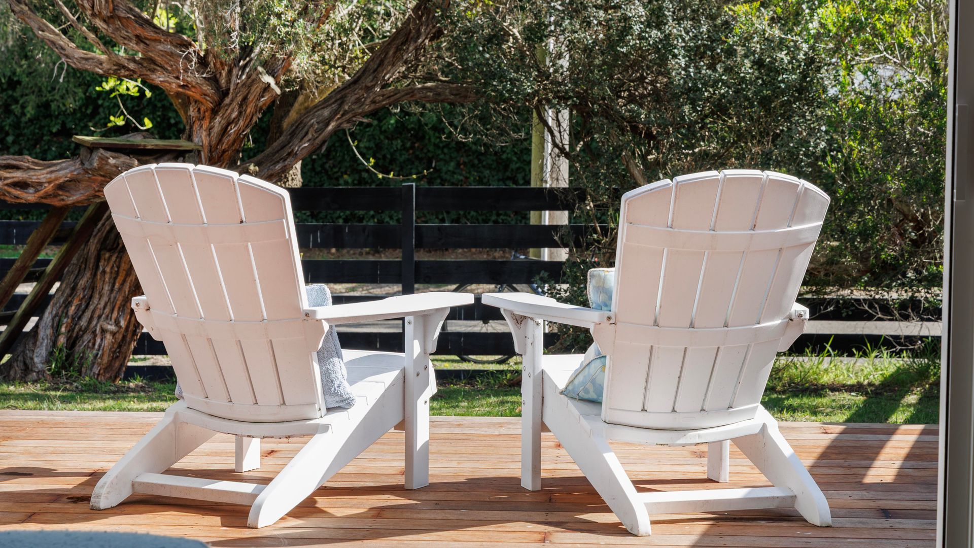 Two Adirondack chairs with a small table between them on a wooden deck.