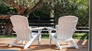 Twee Adirondack stoelen met een kleine tafel ertussen op een houten terras.