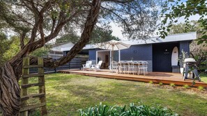 A modern outdoor deck with a dining area, a large tree, and a building with a dark facade. - Casa Della Nonna - Capel Sound (Capel Sound)