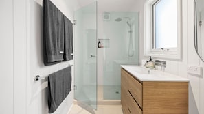 A modern bathroom with a glass shower enclosure, a white vanity with a wooden cabinet, and a window providing natural light. - Casa Della Nonna - Capel Sound (Capel Sound)