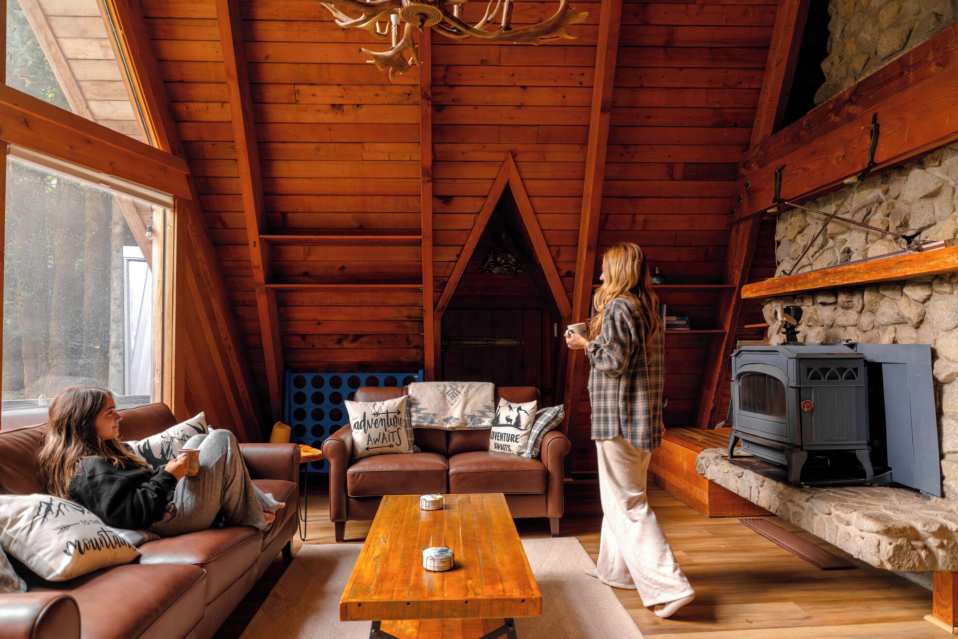 A cozy cabin interior with a fireplace, wooden ceiling, and a stone wall.