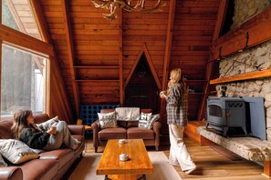 A cozy cabin interior with a fireplace, wooden ceiling, and a stone wall. - Fern Haus  Hiking, Hot Tub & River Access (Gold Bar)