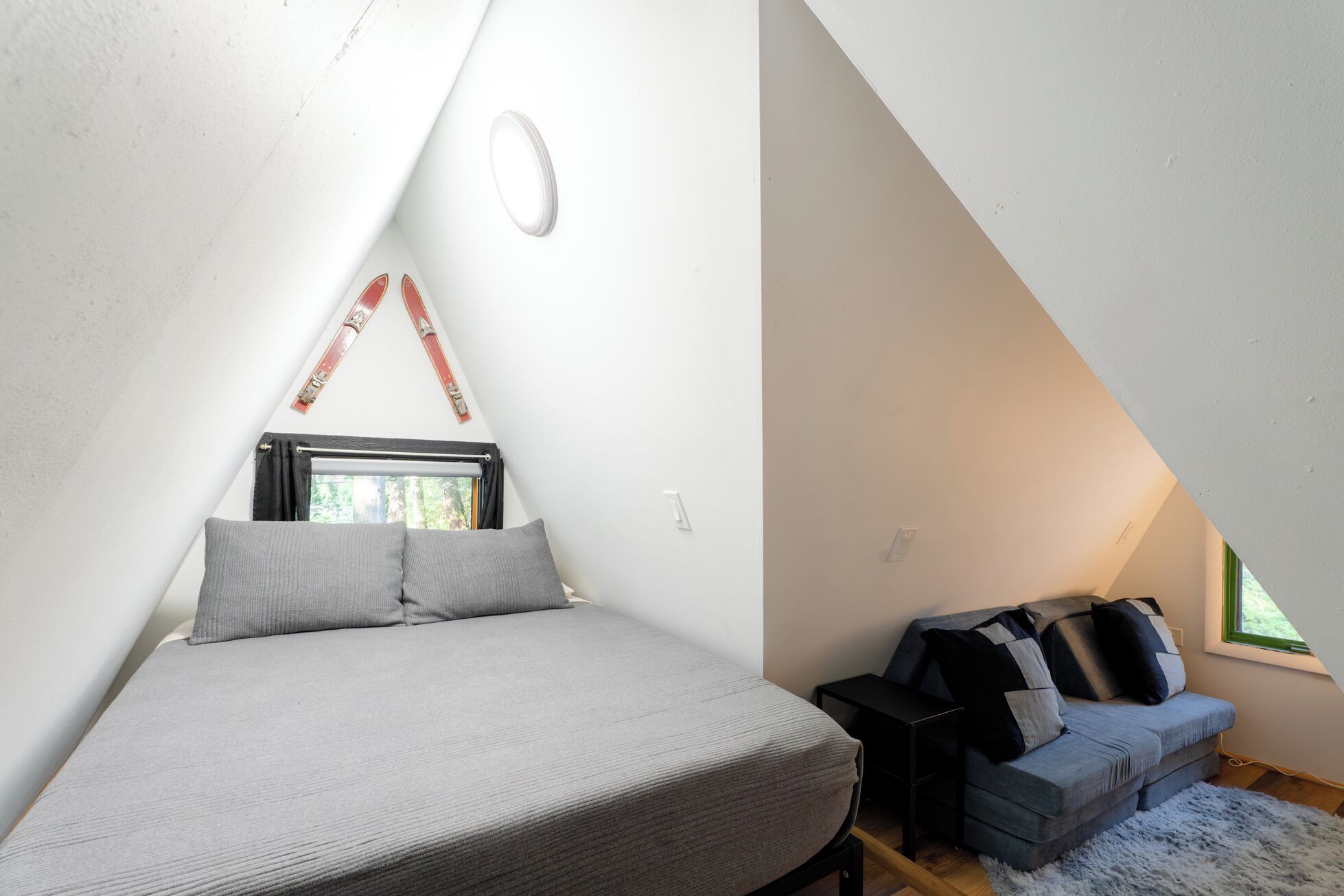 A small, triangular attic room with a bed, a sofa, and a window.