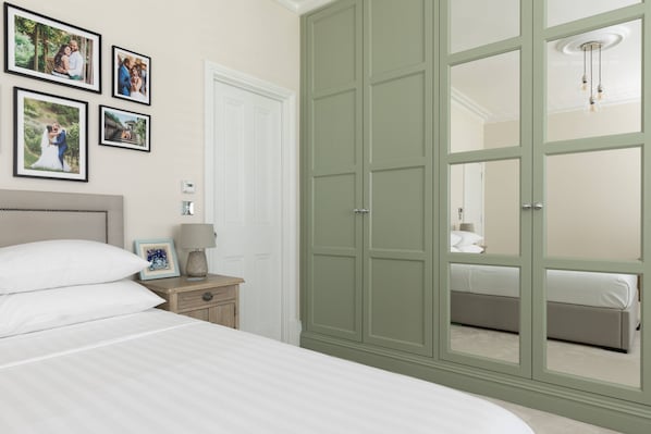 Ein Schlafzimmer mit großem Kleiderschrank, Nachttisch mit Lampe und gerahmten Fotos an der Wand.