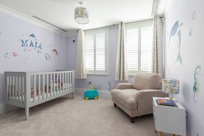 Ein Babyzimmer mit einem Kinderbett, einem Stuhl, einem Spielzeug und einer Wand mit Namen und Dekorationen.