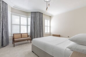 Une chambre à coucher avec un grand lit, un banc et une fenêtre équipée de stores.