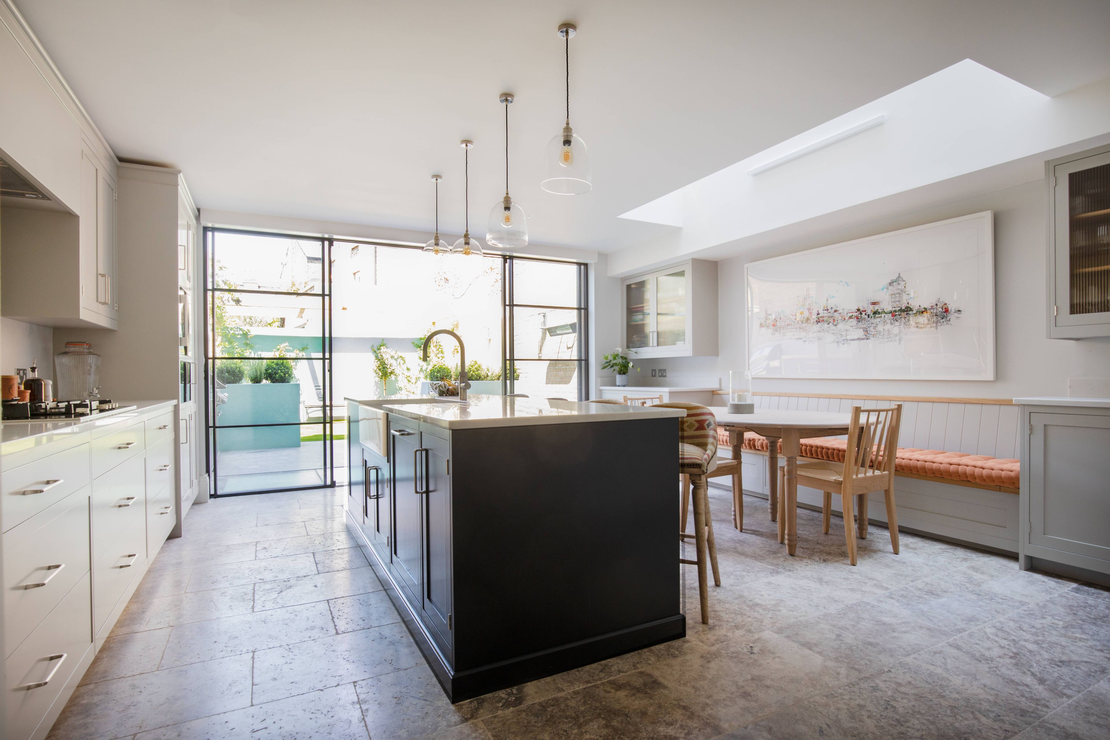 A modern kitchen with a central island, large windows, and a dining area with a bench.