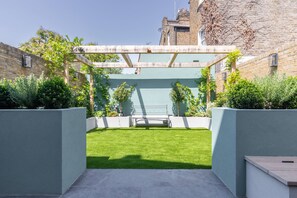 Eine moderne Außenpatio mit grünem Rasen, einer Holzpergola und einer weißen Bank.
