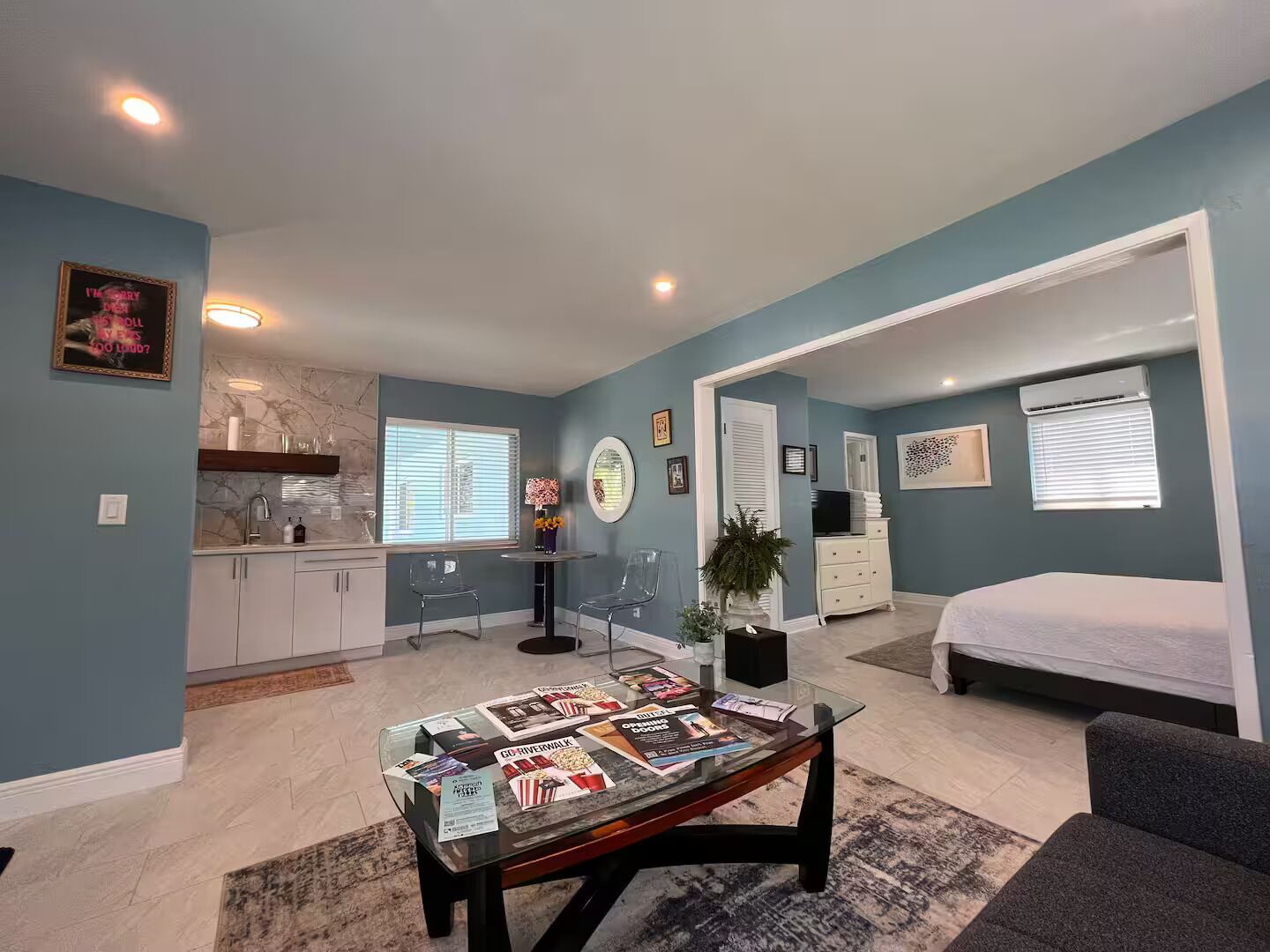 A modern living room with a glass coffee table, a sofa, and a dining area with a kitchen in the background.