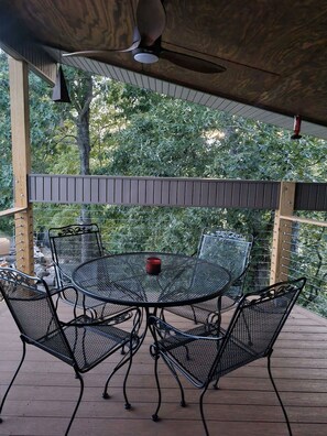 Une terrasse extérieure avec une table ronde en métal et quatre chaises, entourée d’une plateforme en bois et d’une rambarde en métal.