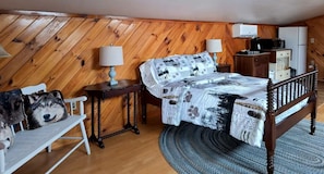 Une chambre confortable avec un plafond en bois, un lit avec une literie à motifs, une table de chevet, une lampe et une chaise ornée d’un motif représentant un chien.