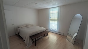 A bedroom with a bed, bench, window with blinds, and a mirror.