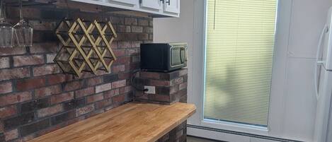 Une cuisine avec un plan de travail en bois, deux tabourets noirs, un mur en briques et des armoires blanches.