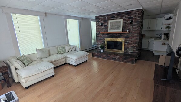 A living room with a sectional sofa, a fireplace, and a kitchen area.