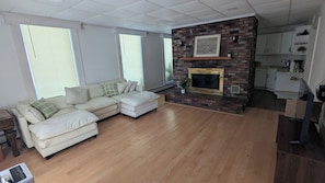 A living room with a sectional sofa, a fireplace, and a kitchen area.