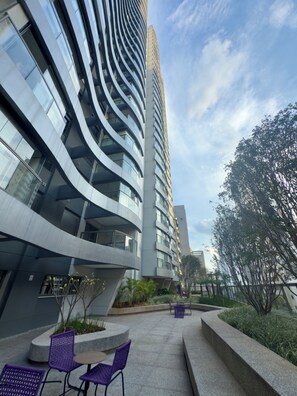 A modern building with curved architecture, outdoor seating, and a clear sky. - Air Brooklin Residence (São Paulo)