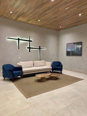 A modern living room with a beige sofa, two blue armchairs, a wooden coffee table, and a rug. - Air Brooklin Residence (São Paulo)