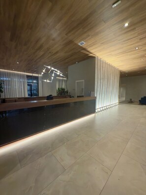 A modern reception area with a wooden ceiling, a black reception desk, and a tiled floor. - Air Brooklin Residence (São Paulo)