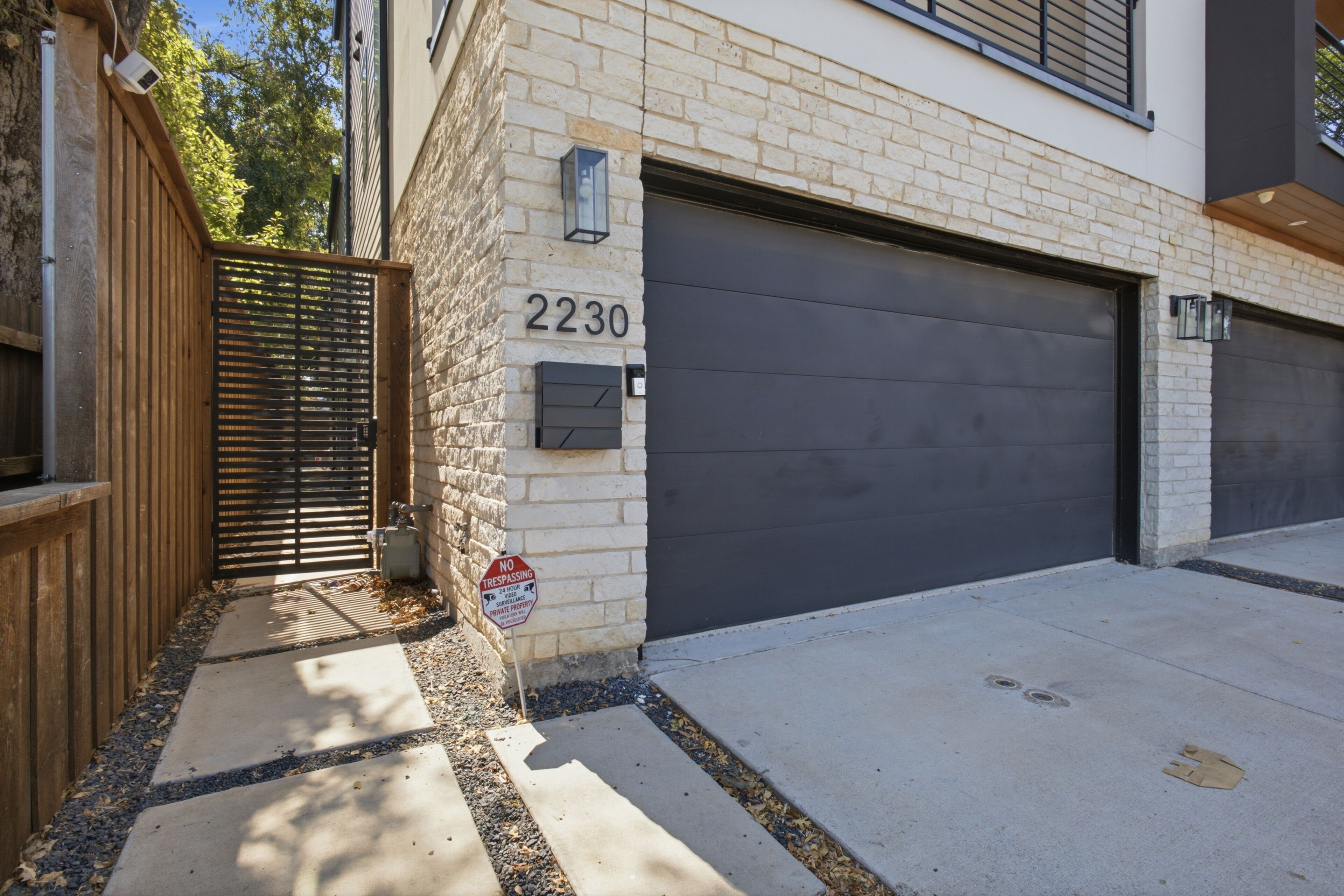A residential garage with a number 2230 garage door, a gated entrance, and a surveillance camera.
