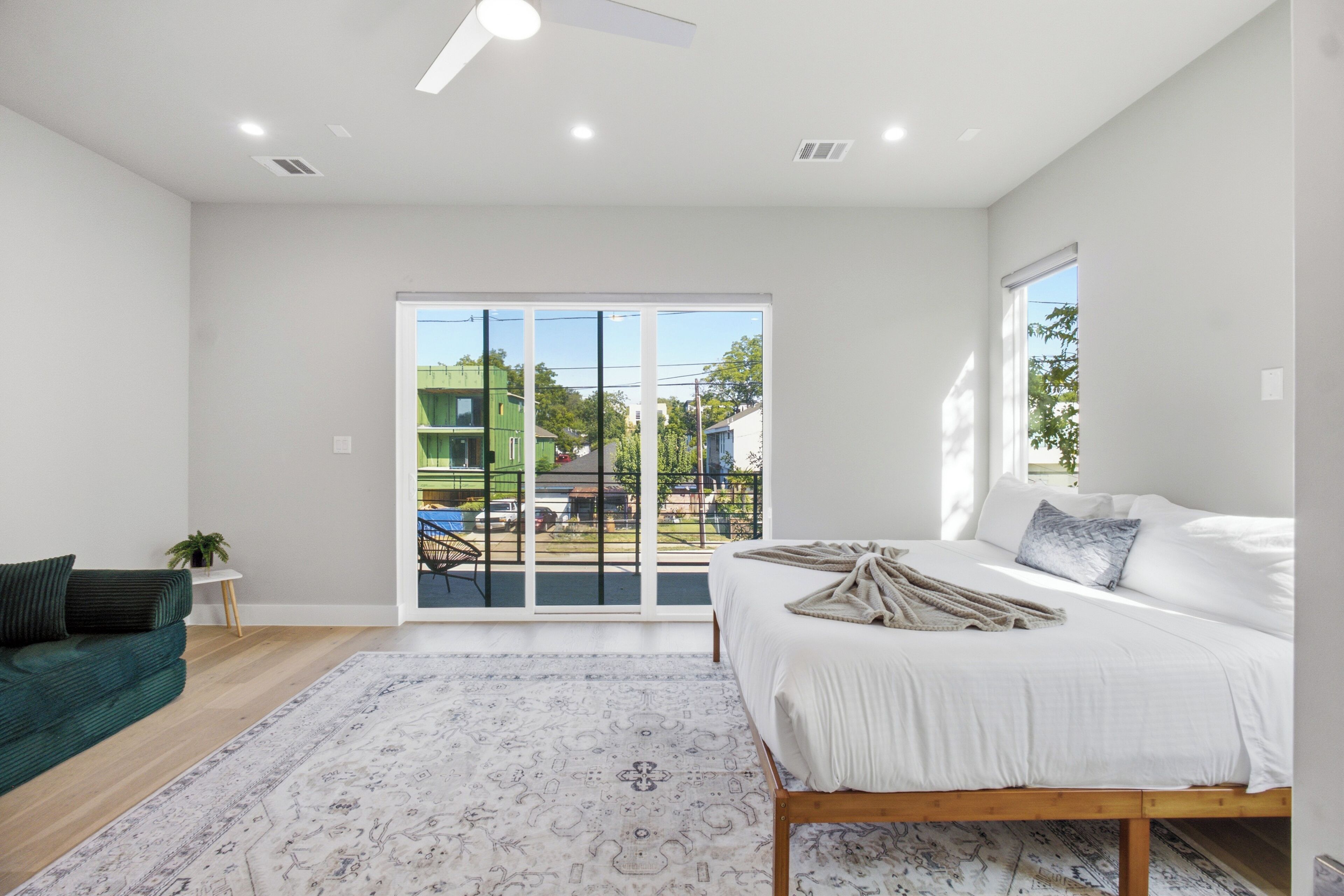 A bedroom with a bed, a window, a door, and a view of the outside.